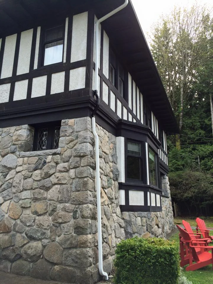 White downspout on a stone and timber home — Aarsen Gutters, Nanaimo BC